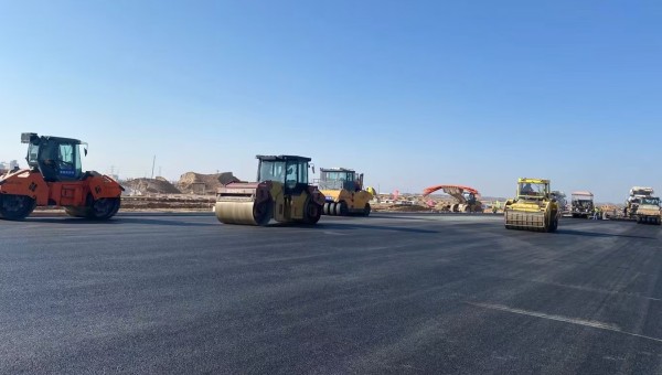 近日，在西部市政建設(shè)集團(tuán)蘭州新區(qū)城市礦產(chǎn)與表面處理產(chǎn)業(yè)園區(qū)（二期）周邊基礎(chǔ)設(shè)施項(xiàng)目—園區(qū)西路南延段（緯五十路至緯二十八路）項(xiàng)目現(xiàn)場，隨著一輛輛運(yùn)料車平穩(wěn)駛?cè)?，攤鋪機(jī)將滾燙的瀝青混合料均勻鋪開，標(biāo)志著項(xiàng)